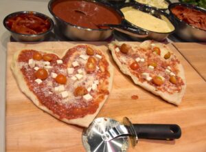 Two heart shaped pizzas with pepperoni and other toppings